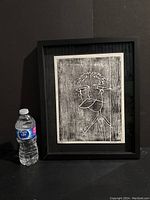 Framed black and white woodblock print displayed next to a water bottle for scale