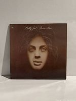 Front cover of Billy Joel Piano Man album LP record showing the distinct sepia-toned face illustration with the title "Billy Joel Piano Man" at top.