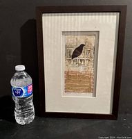 Framed monoprint artwork next to a water bottle for scale showing a bird silhouette on an abstract background.