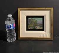 Framed oil on board painting with wood frame and beige matte shown next to a water bottle for scale.