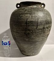 Front view of the large black urn next to a water bottle for scale showing size and texture.