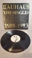 Album cover with gold text 'BAUHAUS THE SINGLES 1981-1983' with vinyl record laid in front