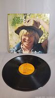 Photo of the vinyl record with cover showing John Denver wearing a hat and glasses, smiling, with a background of greenery.