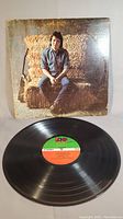 Photo showing vinyl record alongside album cover with John Prine sitting on a haystack, showing wear on cover edges.