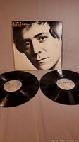 Double vinyl LP records and gatefold cover with close-up of Lou Reed's face visible on the cover. Two black vinyl discs are displayed in front of the cover.