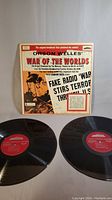 Front view of the War of the Worlds album cover with two vinyl records displayed in front, showing the original broadcast headline artwork on the cover.