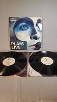 Photo showing the front cover of the Peter Gabriel 'Plays Live' album and two vinyl records laid out underneath.