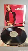 Vinyl record partially out of album cover showing Tom Petty holding a guitar with red background.