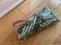 Clear plastic pouch with pink zipper containing multiple assorted crayons seen inside, colors range with visible wear on crayons and wrappers.