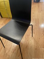 Front angled view of the black chair showing the molded plastic seat and metal legs on a wood floor.