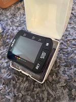 Black Seloy digital wrist blood pressure monitor placed on a textured gray surface showing its screen and buttons