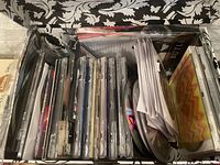 Photo showing a box with multiple DVD and CD cases stacked vertically along with loose discs and paper.
