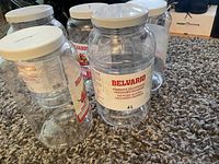 Seven empty clear plastic storage containers with white lids arranged on carpeted floor, visible Belvario label and 4L size indication.