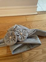 Gray fancy hat laid flat, showing two decorative fabric flowers with pearl bead centers and rhinestone embellishments.