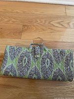Closed flat iron travel organizer bag with green and purple feather pattern, hanging hook, and label.
