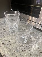 Three clear glasses stacked and placed on granite countertop next to stainless steel appliance.