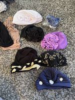 Photo showing nine assorted hats and toques laid on carpet with detail on fabric decorations and colors.