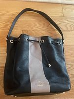 Front view of Kate Spade purse showing black and light gray color block design, drawstring closure, and shoulder strap.