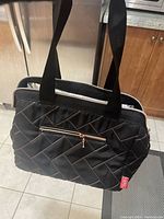 Front and side view of black quilted lunch bag with outer zipper pocket and shoulder straps.