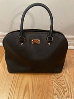 Front view of the black Michael Kors handbag showing dual handles and gold logo plaque.