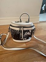 Front view of the small side purse showing the black and white leaf pattern, top handle, and long white strap.