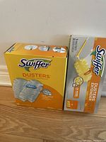 Swiffer Dusters kit with heavy duty extender handle and box of 16 replacement dusting pads shown on wooden floor surface.