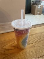 Photo shows a single reusable plastic travel cup with an attached clear lid and clear straw, featuring a colorful abstract pattern.