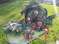 Photo showing artificial Christmas garlands and wreath decorated with pine cones, red berries, and buffalo plaid ornaments placed outside on a table.