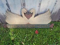 Wooden farmhouse sign showing two swans forming a heart shape with necks, a central heart, and painted phrase 'PEACE TO YOUR HEART' on a rectangular base.