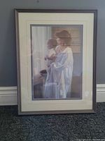 Framed print of a mother holding a baby looking out of a window, soft colors and lighting, with double matte border and brown frame