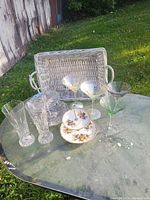 Photo showing assorted glassware on outdoor table including three martini glasses in different colors, two cut crystal water glasses, and a two-tier floral serving dish.