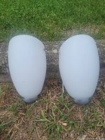 Pair of matching frosted white glass wall sconces placed on grass ground.