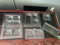Five clear textured glass serving platters displayed on a dark glass surface, varying in sizes and compartmentalization, all matching in style.