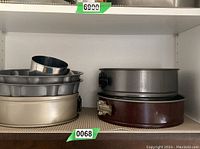 Photo showing a stack of various metal baking molds including several springform pans with latch closures and round cookie cutters, all in silver and dark colors.