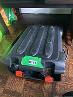 Closed black plastic carrying case with textured surface and red latch closures, placed on wooden floor surface.