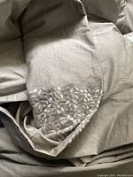 Close-up of beige duvet fabric with white embroidered leaf pattern detail on edges.
