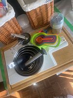 Photo showing stainless steel mixing bowls nested, plastic measuring cups and spoons, white and wooden cutting boards, mason jar with scooper, and one wicker basket
