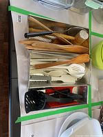 Wooden spoons, plastic spoons, meat mallet, and organizer containers on table.