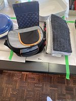 Photo of gray and black Thermos insulated lunch bag with orange trim alongside fabric napkins with checked patterns.