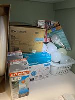 Boxed LED light bulbs and loose bulbs in basket shown on table.