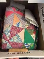 Colorful patchwork quilt folded inside a box alongside white fabric