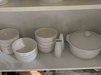 Set of white bowls stacked in groups with a tall serving bowl covered by a lid. The bowls and serving bowl have a smooth, glossy finish.