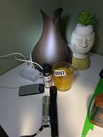 Photo showing Sage Aroma Geni diffuser, yellow candle, lavender oil, remote control, two flashlights, and a power adapter on a white table next to a decorative planter