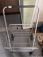 Top-down view showing inside of grey metal shopping cart with mesh bottom and black handle grip.