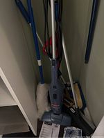 Blue Bissell Magic Vac stick vacuum with accessories and cleaning tools around it including duster and mop, user manual and packaging.