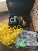 DeWalt cordless drill, charger, battery, yellow rope and MasterCraft ratchet screwdriver set in clear case on floor.