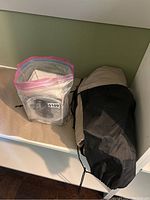 Twin air mattress in a black and beige carrying bag next to a sealed plastic bag containing the pump box.