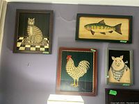 Four framed wooden panel paintings of farm animals (cat, fish, chicken, pig), hung on a purple wall.