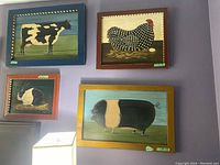 Four framed folk art animal paintings displayed on wall: cow, chicken, rabbit, pig