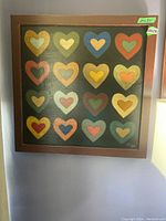 Frontal view of the square wooden framed heart art painting featuring 16 colorful hearts on a black background.